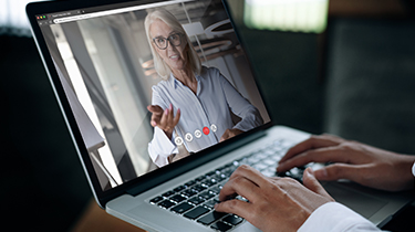 A businessman speaks on a web conference with an advisor using a laptop webcam.