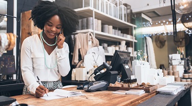 Black female storeowner taking a customer order over the phone.