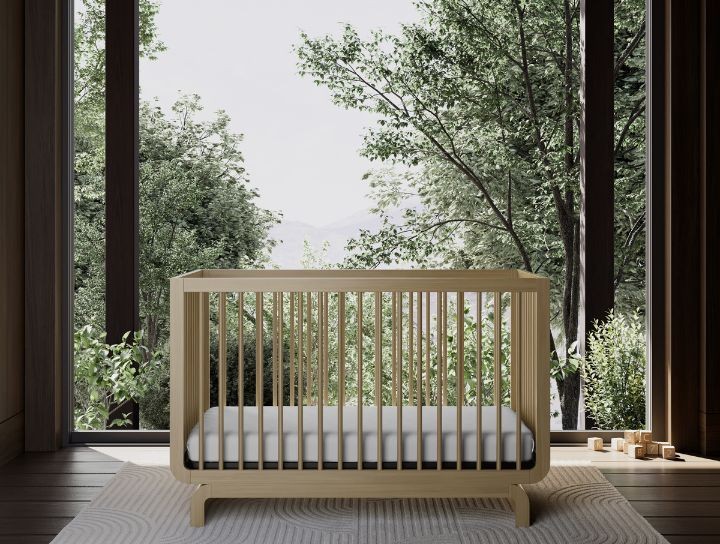 A minimalist wooden baby crib in a bright room with large windows and trees outside