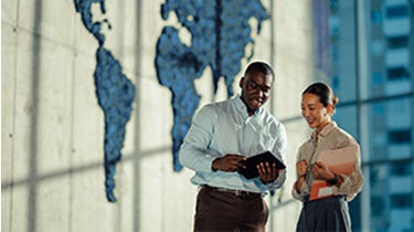 Two business colleagues discuss global strategies in a modern office with a large blue world map.
