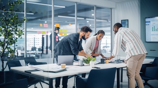 A group of people standing around a table in an office planning their business growth to the Indo-Pacific