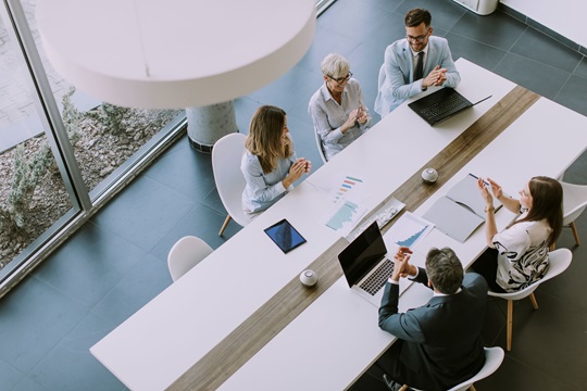 Bird's eye view of office workers clapping hands as they sit around a boardroom table