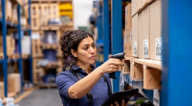 Un employé scanne les stocks au moyen d’un lecteur de codes-barres et d’une tablette dans une allée d’entrepôt.
