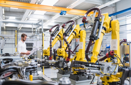 Young engineer reading paper while standing by robotic arms in automated industry