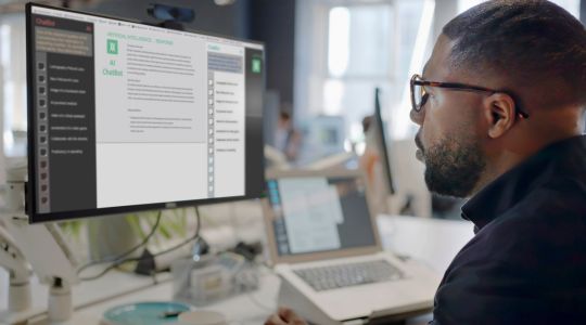 Un homme regardant un écran d’ordinateur où l’on peut voir un agent conversationnel alimenté par l’intelligence artificielle.