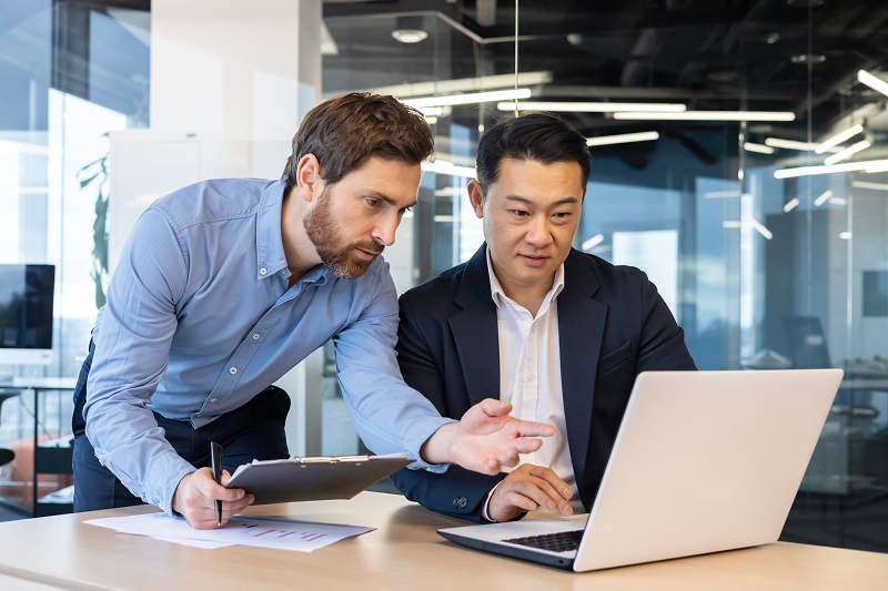 Two business professionals discussing strategy at a table with documents and a laptop.
