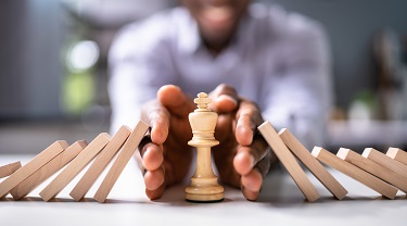 Man’s hands cradle chess piece as dominos fall