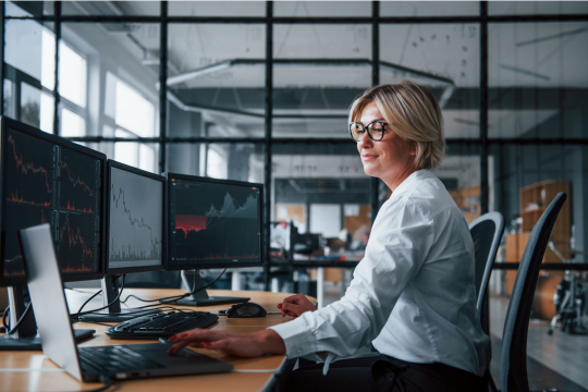 A woman looking at financial metrics across multiple computer screens. 