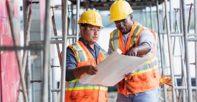 Deux ouvriers du bâtiment multiethniques en équipement de sécurité examinent les plans