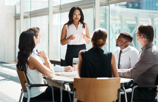 Une femme debout dans un bureau moderne faisant une présentation lors d’une réunion avec des collègues