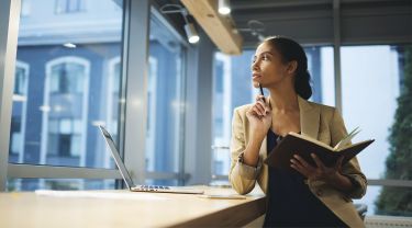 Une femme d'affaires tenant un cahier et un stylo, regardant par la fenêtre d'un bureau.