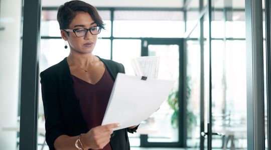 Une femme d'affaires en tenue professionnelle examine des documents dans un bureau.