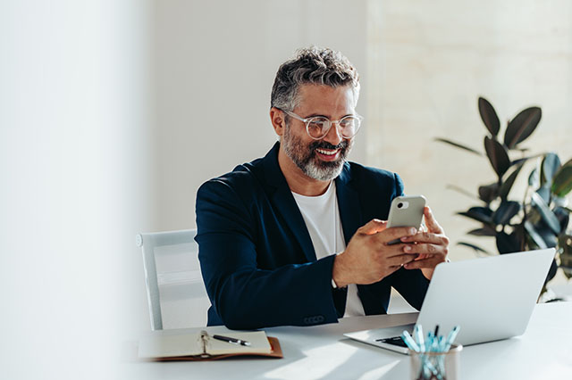 A cheerful, mature professional man in his office looking confidently at his smartphone.