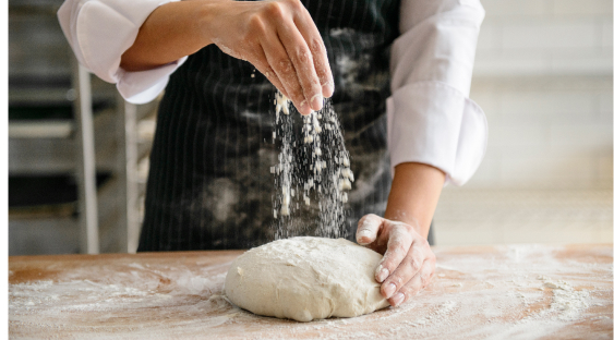 A baker dusting flour on a dough to make bread.