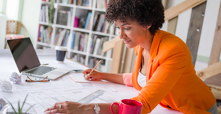 Woman writing on a notepad while working at her desk with a laptop.