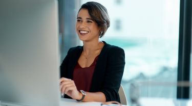Une femme d’affaires arborant un sourire travaille à son ordinateur, dans un bureau.