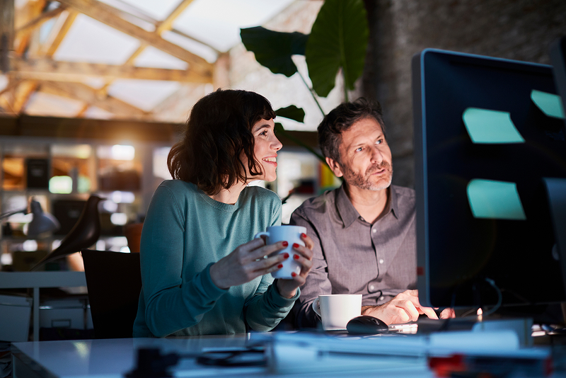 Deux personnes travaillant ensemble dans un bureau moderne, avec un écran d’ordinateur et des tasses à café.