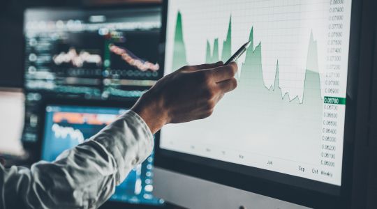 Close-up of a businessman pointing with a pen to data on a chart displayed on a computer screen.