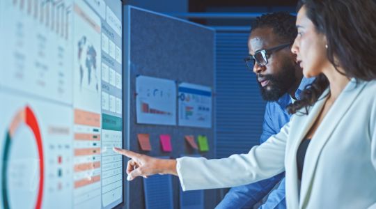 A man and a woman reviewing data displayed on a board.