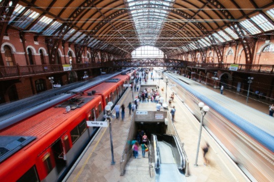 A busy train station with one train stopped and one blurred as it leaves the station