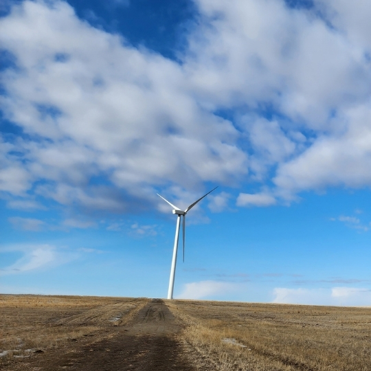 Une turbine éolienne se dressant dans un champ à ciel partiellement nuageux.