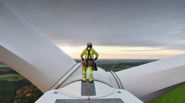 Technicien sur corde debout sur le moyeu d’une éolienne au lever du soleil