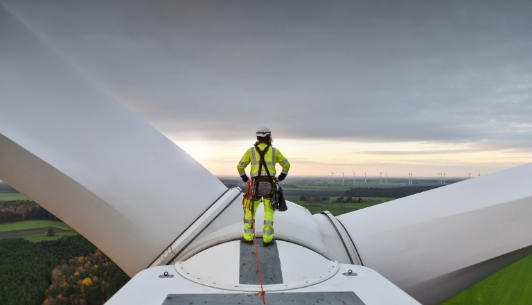 Technicien sur corde debout sur le moyeu d’une éolienne au lever du soleil