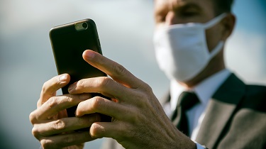 Un homme d’affaires portant un masque chirurgical envoie un message texte avec son téléphone cellulaire.