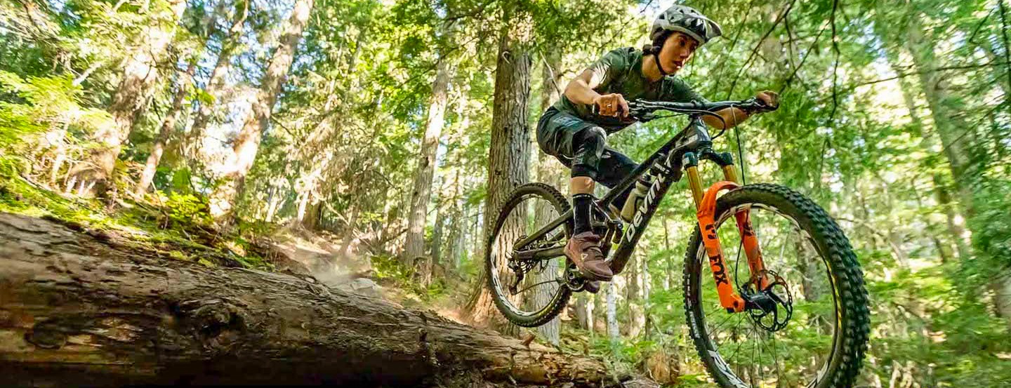 Cyclist rides high over a hill on a Devinci mountain bike.