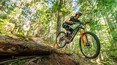 Cyclist rides high over a hill on a Devinci mountain bike.