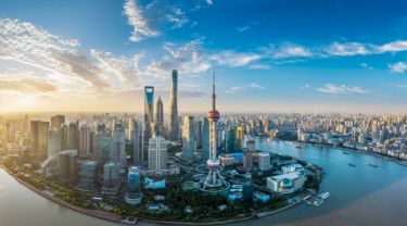 Aerial view of Shanghai’s modern skyline, with tall skyscrapers along a winding river under a bright blue sky.