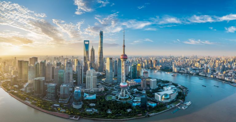 Aerial view of Shanghai’s modern skyline, with tall skyscrapers along a winding river under a bright blue sky.
