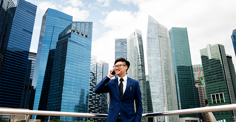 Smiling Asian man stands in front of Bangkok skyscrapers