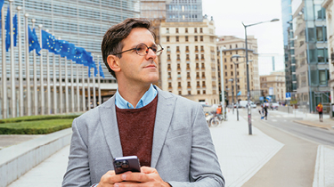 Business person standing outside a building with European Union flags, symbolizing access to European markets.