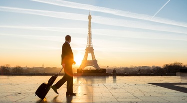 Beautiful sunrise over Paris behind Eiffel Tower as a businessman walks with luggage.