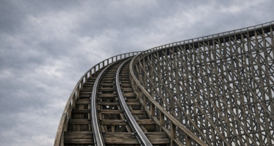 Wooden rollercoaster track stretches upward into a dark, gloomy sky.