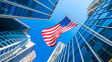 USA flag waving in the wind with contemporary glass buildings in the background.