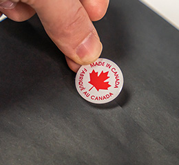 Gros plan des mains d'un propriétaire de petite entreprise apposant un autocollant « Made in Canada » sur une marchandise.