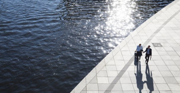 Two business partners walking beside a lake. One man is pulling a suitcase while the other is holding a briefcase.