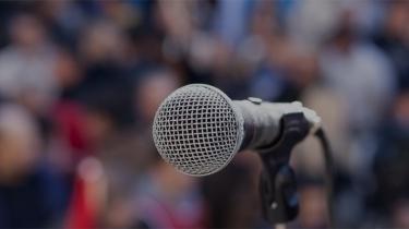 Un microphone devant une foule ombragée représente les risques politiques parfois cachés pour les entreprises.