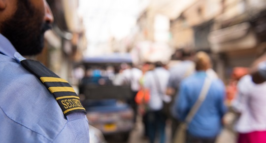 A security officer looks over the crowd in a busy outdoor marketplace.