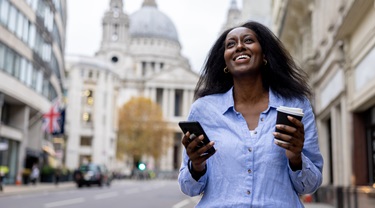 Femme d'affaires souriante vérifiant son téléphone portable dans une rue urbaine en Grande-Bretagne