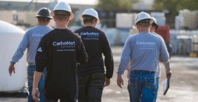 Five men wearing construction hats and CarboNet shirts walking outdoors, facing away from the camera.