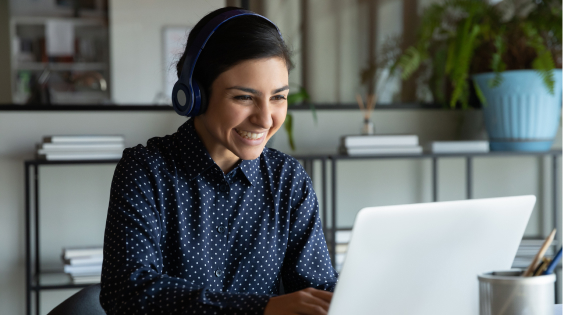 Person sitting at table on laptop computer looking at the screen and wearing headphones