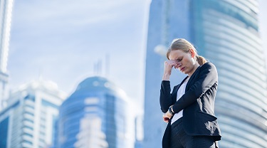 Stressed businesswoman looks upset and holds head in her hand outside of her workplace.