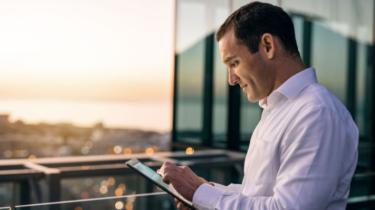 Exporter studies tablet on balcony looking over city skyline